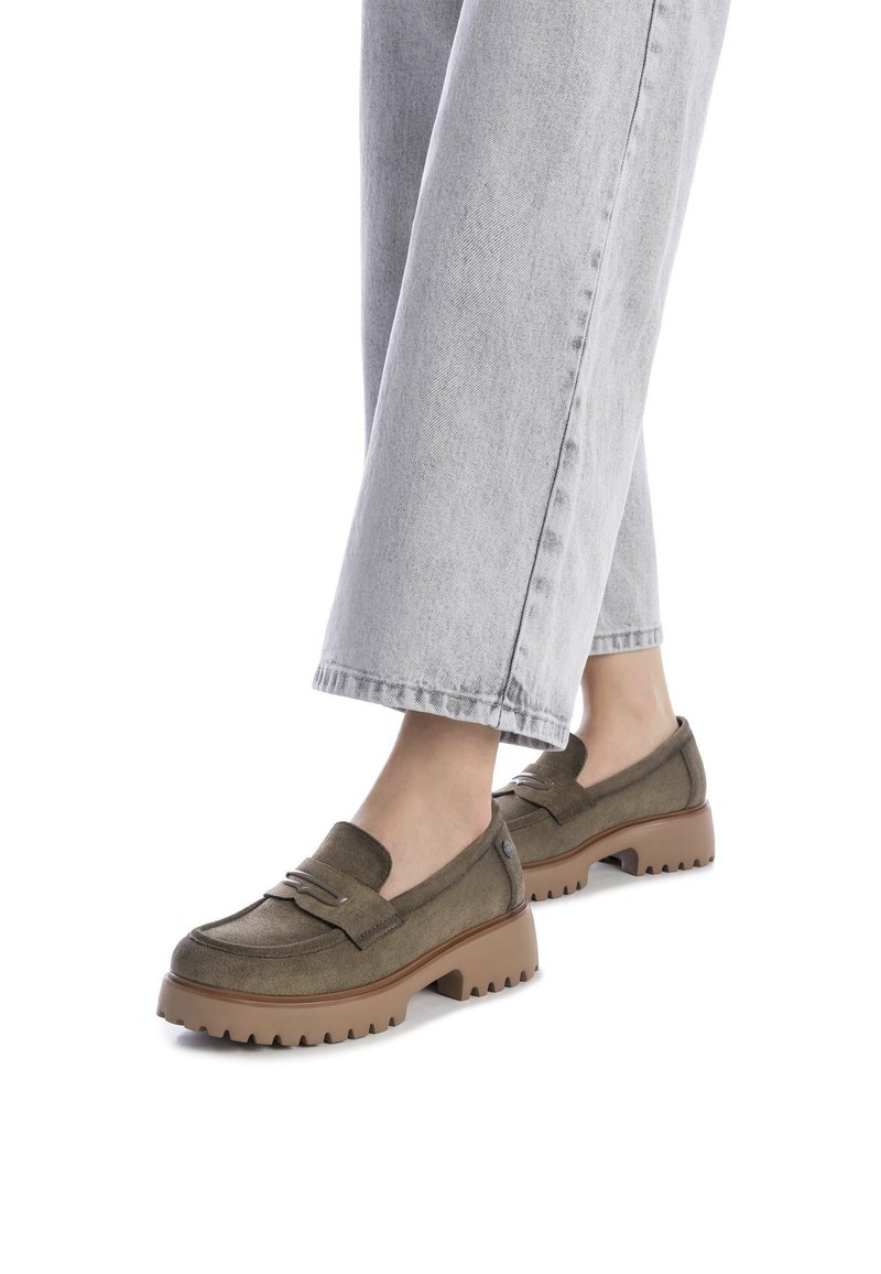 Mocasines de ante verde aceituna con un marcado detalle de costura, una suela de color marrón acolchada y gruesa, y un ligero tacón, combinados con unos vaqueros de denim gris claro.