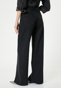 Pantalones vaqueros de pierna ancha en negro, hechos de denim, con una cintura alta, dos bolsillos traseros y un dobladillo ligeramente acampanado con bordes deshilachados.