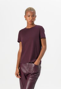 T-shirt bordeaux à manches courtes en tissu doux avec un col rond, porté avec un pantalon en cuir bordeaux taille haute.
