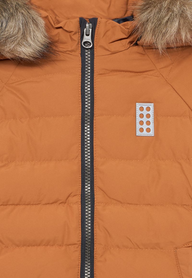 Gestepptes oranges Jacket mit einem marineblauen Reißverschluss, ausgestattet mit einer fellgefütterten Kapuze und einem rechteckigen Logo-Patch mit sechs Löchern auf der Brust.