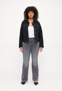 Črna jeans jakna s sprednjimi gumbi, v kombinaciji s sivimi širokimi hlačami. Črne čevlje s koničastimi prsti dopolnjujejo videz.