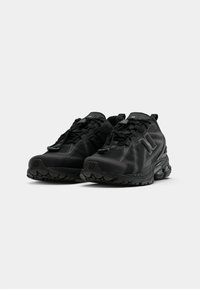 Baskets de sport noires avec une tige texturée, un design à lacets, une semelle en caoutchouc et des accents réfléchissants. Elles disposent d'une semelle rembourrée pour un soutien optimal.