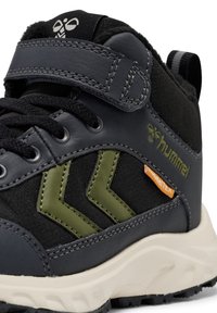 Zwarte en olijf hoge sneaker met klittenbandsluiting, veters, witte zool en "hummel" logo aan de zijkant met een oranje label.