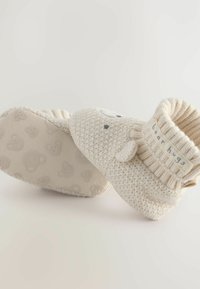 Pantofole lavorate a maglia color crema con polsino a coste, suola testurizzata con facce d'orso e un'etichetta ricamata che reca la scritta "abbracci d'orso."