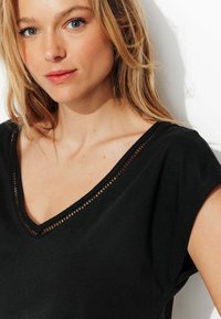 Un haut noir à manches courtes avec un décolleté en V et une bordure en tissage décoratif. Fabriqué en tissu lisse, mettant en avant une coupe décontractée.