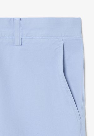 Primo piano di tessuto azzurro chiaro che mostra la vita con passante per cintura e dettaglio della tasca frontale inclinata sui pantaloni.