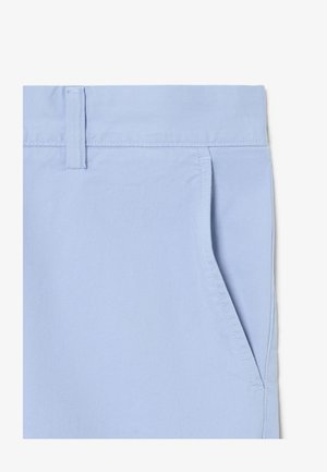 Primo piano di tessuto azzurro chiaro che mostra la vita con passante per cintura e dettaglio della tasca frontale inclinata sui pantaloni.