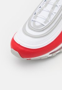 Sneaker con tomaia in rete bianca, accenti in pelle rossa e dettagli grigi. Presenta una suola ammortizzata e un design stratificato e curvato.