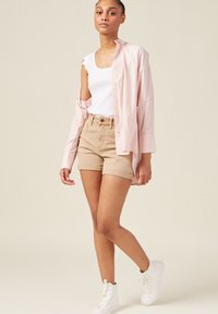 Ljusrosa skjorta med knappar över en vit ribbad linne, kombinerat med beige uppvikta shorts och vita höga sneakers.