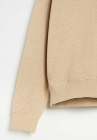 Beżowy sweatshirt o miękkiej teksturze, z prążkowanymi mankietami i dołem. Projekt charakteryzuje się luźnym krojem i minimalnymi detalami przeszyć.
