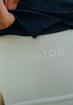 Zwarte gestructureerde stoflaag over een witte gladde stof. Het woord "ACTIVATOR" is in het wit gecastreerd in de onderste sectie.