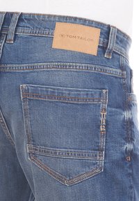 Niebieskie dżinsy z denimu z skórzaną metką na pasie. Cechy to tylne kieszenie z kontrastującym przeszyciem oraz fakturowane wykończenie.