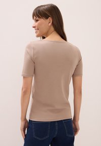 Beige košile s krátkým rukávem a kulatým výstřihem, vyrobená z měkké látky. Hladký střih, jemná textura a lemování, které sahá pod pas.