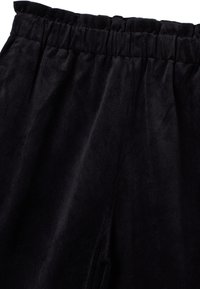 Pantaloni in velluto a coste neri con superficie testurizzata, dotati di cintura elastica e tasche laterali, progettati per il comfort e la facilità d'uso.