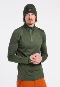 Olivengrüner, langärmeliger Pullover mit Viertelreißverschluss, strukturiertem Finish und Logo, kombiniert mit einer passenden Strickmütze.
