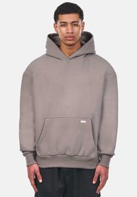 Kapuzensweatshirt in dezentem Grau, mit einer Vordertasche, gerippten Bündchen und Saum. Weicher Stoff, lockere Passform, minimale Markierung auf der Vorderseite.