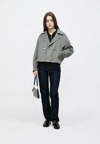 Kuttet grå dobbelspent jakke med gullknapper, brukt over en svart topp, kombinert med mørke jeans og en liten teksturert håndveske.