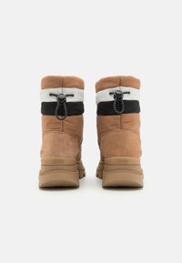 Brązowe zamszowe botki za kostkę z wyściełanym wierzchem w kolorze kremowym, czarnym i brązowym. Posiadają zapięcie na sznurki oraz teksturowane gumowe podeszwy.