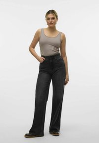 Szary tank top, czarne spodnie z wysokim stanem, szerokie nogawki, widoczne szwy i masywne czarne buty z brązowymi podeszwami. Jednolity biały tle.