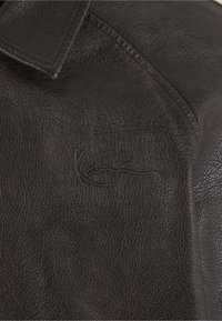 Geacă maro din piele cu finisaj texturat, cu guler decupat și un logo în relief pe partea stângă.