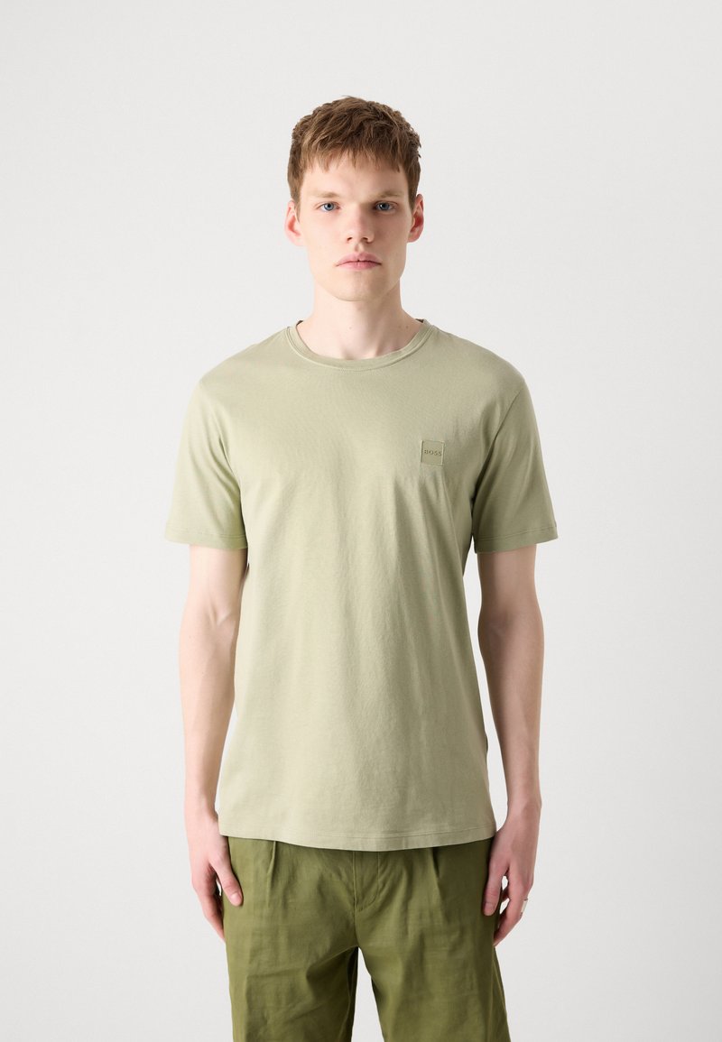 T-shirt vert clair à manches courtes en coton avec un col rond et une petite étiquette de marque sur la poitrine gauche. Texture lisse, design simple.