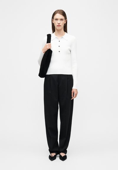 Γυναίκα που φοράει λευκό μακρυμάνικο πουκάμισο πόλο με κουμπιά, μαύρο φαρδύ παντελόνι, μαύρα μπαλαρίνες και κρατάει μαύρη τσάντα ώμου με υφή.