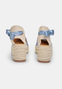 Espadrilové podpätky z tkaného béžového textilu s modrými saténovými akcentmi. Obsahujú hrubú šnúrovú podrážku a mašľový detail na zadnej strane.