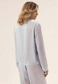 Jedwabista jasnoniebieska bluzka z długimi rękawami, kołnierzykiem i luźnym krojem. Gładka tekstura, minimalistyczny design i brak widocznych wzorów.