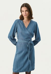 Robe portefeuille en denim bleu clair avec des manches longues, un col en V et une ceinture nouée à la taille. Présente une texture lisse et une ligne d'ourlet droite.