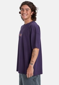 Lilla bomulds T-shirt med korte æermer, en afslappet pasform og broderet detaljer på brystet. Synlige blomster- og kirsebærtatoveringer på armen.