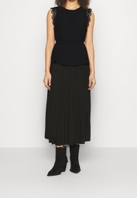Černý peplum top s krajkovým lemem, spárovaný s dlouhou, plněnou tmavě zelenou sukní a černými semišovými kotníkovými botami. Jednoduchý, elegantní silueta.