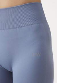 Világoskék, magas derekú leggings, bordázott derékrésszel és sima textúrával, oldalt finom logóval és légáteresztő oldalpanelekkel.