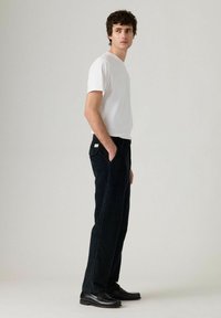 Pantaloni a scacchi neri con taglio dritto, abbinati a una t-shirt bianca a maniche corte e mocassini neri. Dettagli di design minimi.