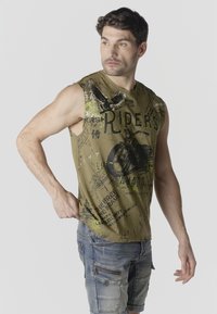 Hombre con camiseta sin mangas verde oliva con gráfico de motocicleta y texto "RIDERS", combinado con pantalones cortos cargo de mezclilla azul.
