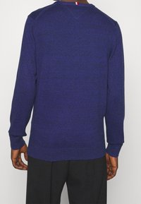 Maglione viola a maglia con maniche lunghe, polsini a coste e scollatura rotonda con un piccolo accento rosso, bianco e blu sul retro.