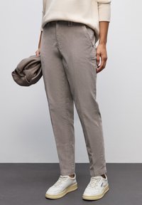 Ljusbeige bomullsbyxor med smal passform, som har sidofickor och en mjuk textur, i kombination med vita sneakers.