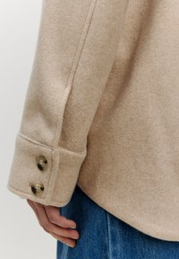 Beige Hemd aus Wollmischung mit strukturiertem Stoff, ausgestattet mit einem abgerundeten Manschette mit zwei transparenten Knöpfen und einer taillierten Silhouette.