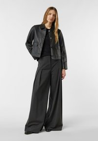 Czarna skórzana krótka kurtka z kołnierzem i zapięciem na guziki z przodu, zestawiona z szarymi spodniami o szerokich nogawkach, z przodu z zakładkami i gładką fakturą.