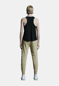 Schwarzes ärmelloses Tanktop, kombiniert mit beigen Jogginghosen mit gerippten Bündchen, Taschen und einem Logodetail nahe dem Knöchel.