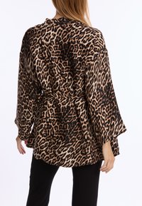 Leopardenmuster Kimono-Robe. Aus weichem Stoff gefertigt, mit langen Ärmeln, einem gebundenen Taillenbund und einer fließenden Silhouette auf schwarzem Hintergrund.