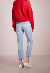 Röd stickad tröja, ljusblå slitna jeans och vita skor med metalliska accenter. Avslappnad passform och uppfransade fållar är synliga.