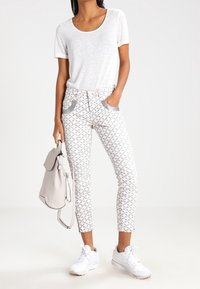 Camiseta blanca de manga corta combinada con pantalones cortos grises y blancos de patrón que tienen bolsillos frontales. Zapatillas blancas y un bolso ligero gris.