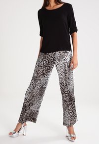 Top nero a maniche corte abbinato a pantaloni larghi grigi con stampa leopardata e sandali alti argentati. Tessuto liscio e vestibilità rilassata.