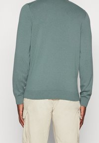 Grön tröja med långa ärmar, ribbstickade manschetter och nederkant. Mjuk textur, figurnära design och rundad halsringning. Bärs över ljus beige byxor.