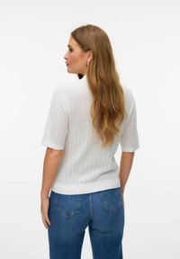 Top in maglia bianca a maniche corte con un motivo testurizzato, dotato di scollatura rotonda e orlo a coste. Abbinato a jeans in denim blu.