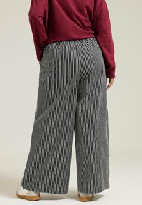 Breda byxor med vertikala svart- och vitrandiga mönster, med ett elastiskt midjeband och en flytande design. Tillsammans med en vinröd långärmad topp.