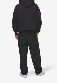 Svart bomullshoodie med en avslappnad passform, tillsammans med löst sittande svarta denimbyxor med dubbla bakfickor och en subtil logodetalj.