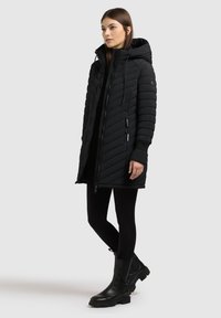 Black padded coat with chevron stitching, hood, front zipper, and side pockets. Paired with black leggings and ankle boots.