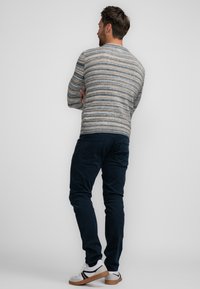 Pull en tricot avec des rayures horizontales beige, bleu et gris, associé à un pantalon slim-fit bleu marine et des baskets blanches avec des accents noirs.