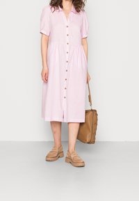 Jasnoróżowa krótko rękawowa sukienka zapinana na guziki z falbaniastej spódnicy, z drewnianymi guzikami, w zestawieniu z beżowymi zamszowymi butami i brązową torebką.